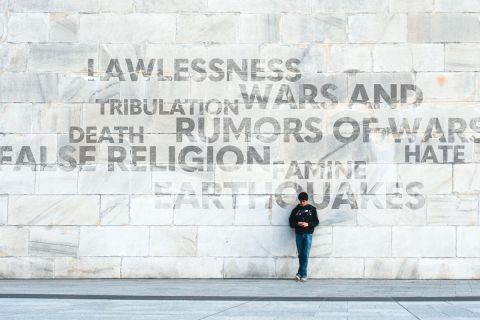 Person standing in front of a large wall displaying negative words associated with the end times, to illustrate the article 